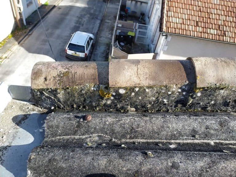 Tuiles faîtières anciennes avec lichen et mortier dégradé, vue plongeante sur une rue et une voiture.