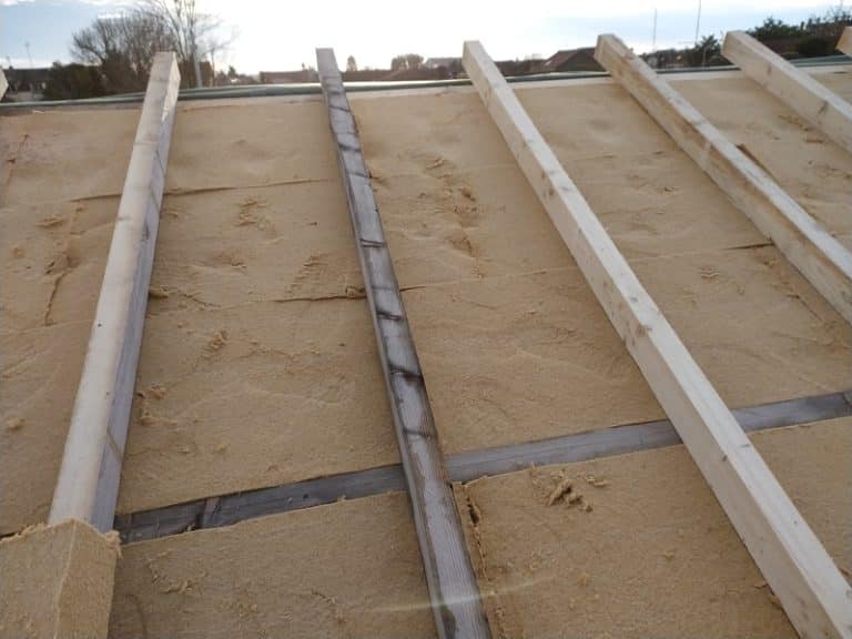 Pose de panneaux d'isolation thermique sur une toiture avec chevrons en bois apparents lors d'une rénovation.