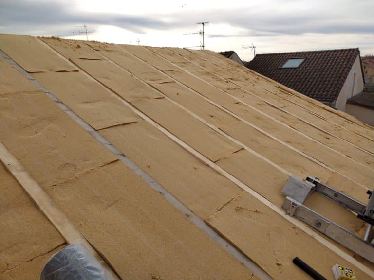 Pose de panneaux isolants en fibre de bois entre les chevrons d'une toiture en cours de rénovation énergétique.