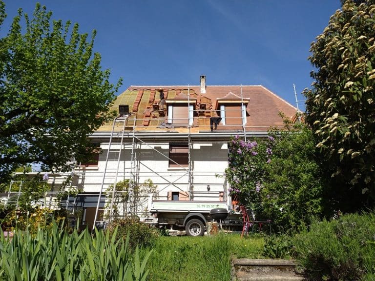Artisans couvreurs rénovant la toiture d'une maison avec échafaudage sous un ciel bleu ensoleillé.