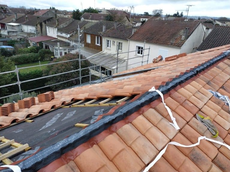 Pose de tuiles rouges et membrane Figaroll Plus sur un toit en rénovation avec échafaudage en arrière-plan.