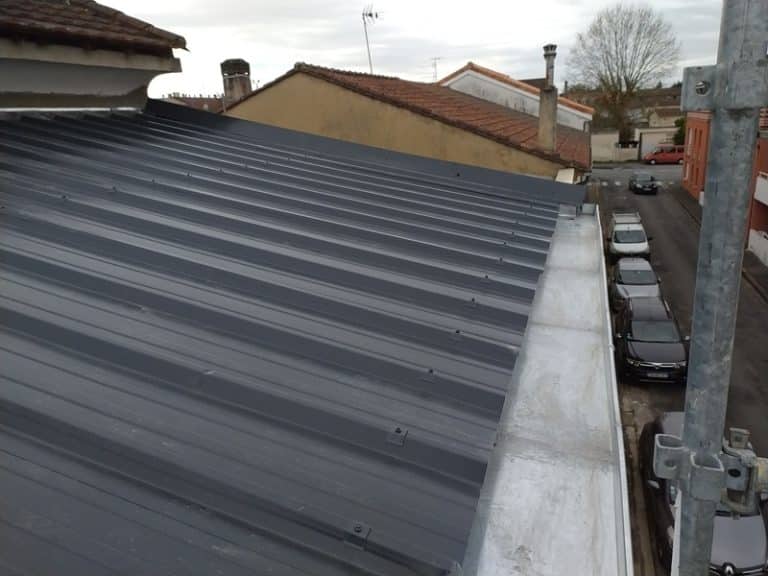 Toiture en tôle ondulée gris anthracite avec chéneau métallique au-dessus d'une rue avec voitures garées.