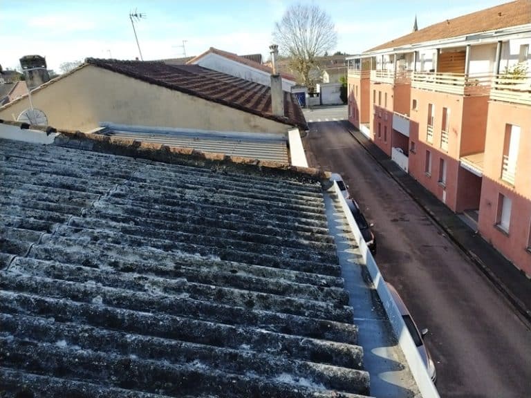 Toiture en plaques de fibrociment ondulées usées et vieillissantes dominant une rue urbaine avec immeubles.